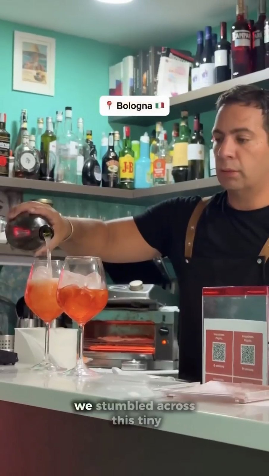 Barman Crunchy che versa due spritz al banco con QR sul bancone